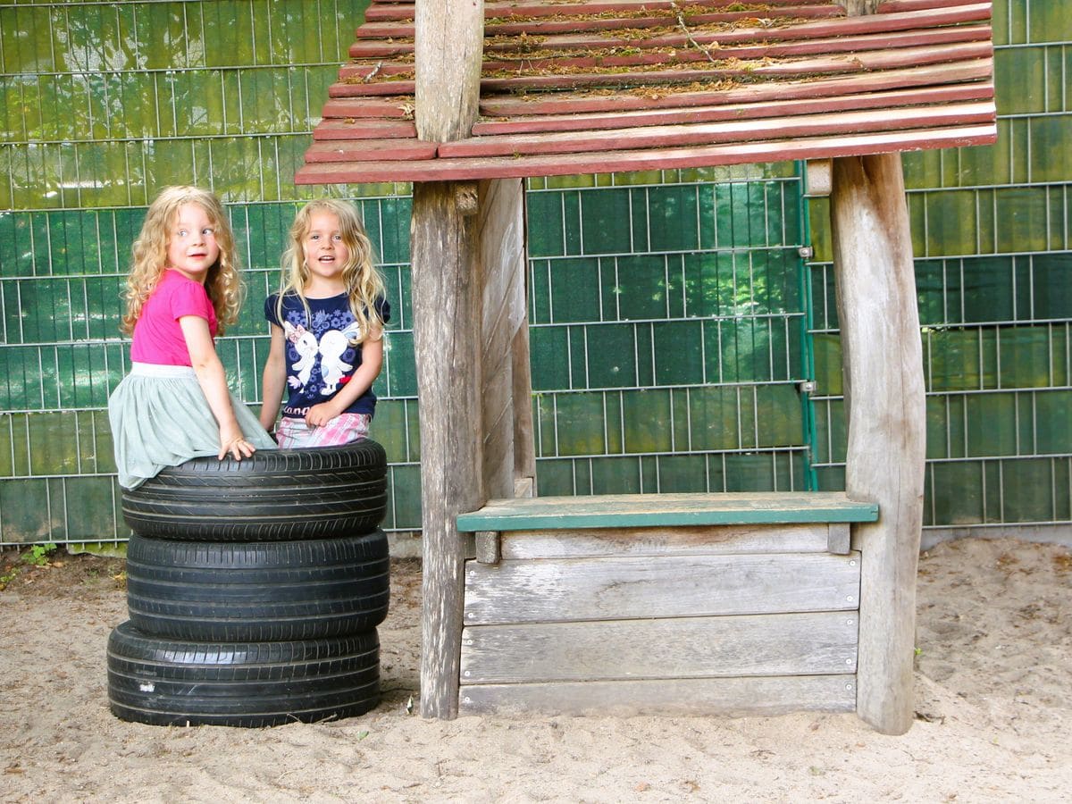 Zwei Kinder spielen an einer Holzbank im Garten des Kindergartens.
