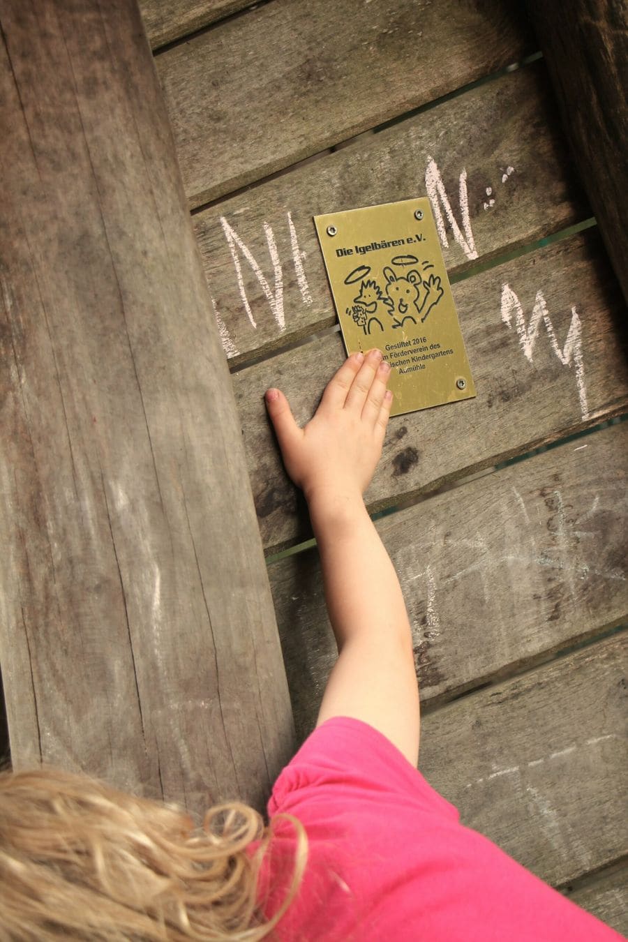 Ein Kind berührt das handgemalte Holzschild der Igelbären am Kindergarten.